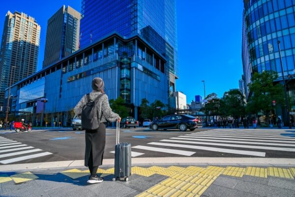 都会の交差点で、スーツケースを持っている後ろ姿の女性の画像